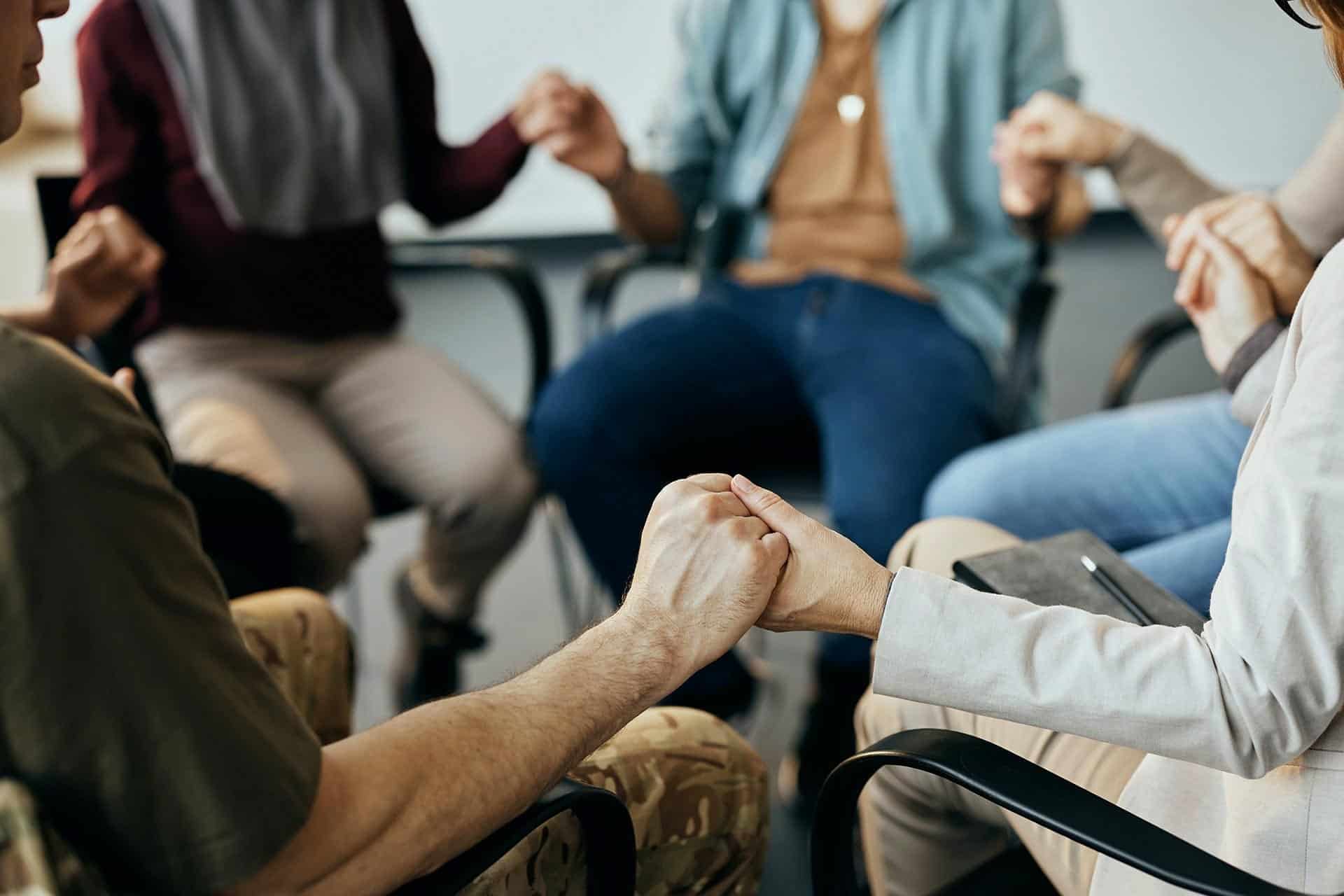 Hand-in-hand support during group therapy session for emotional healing and mental health.